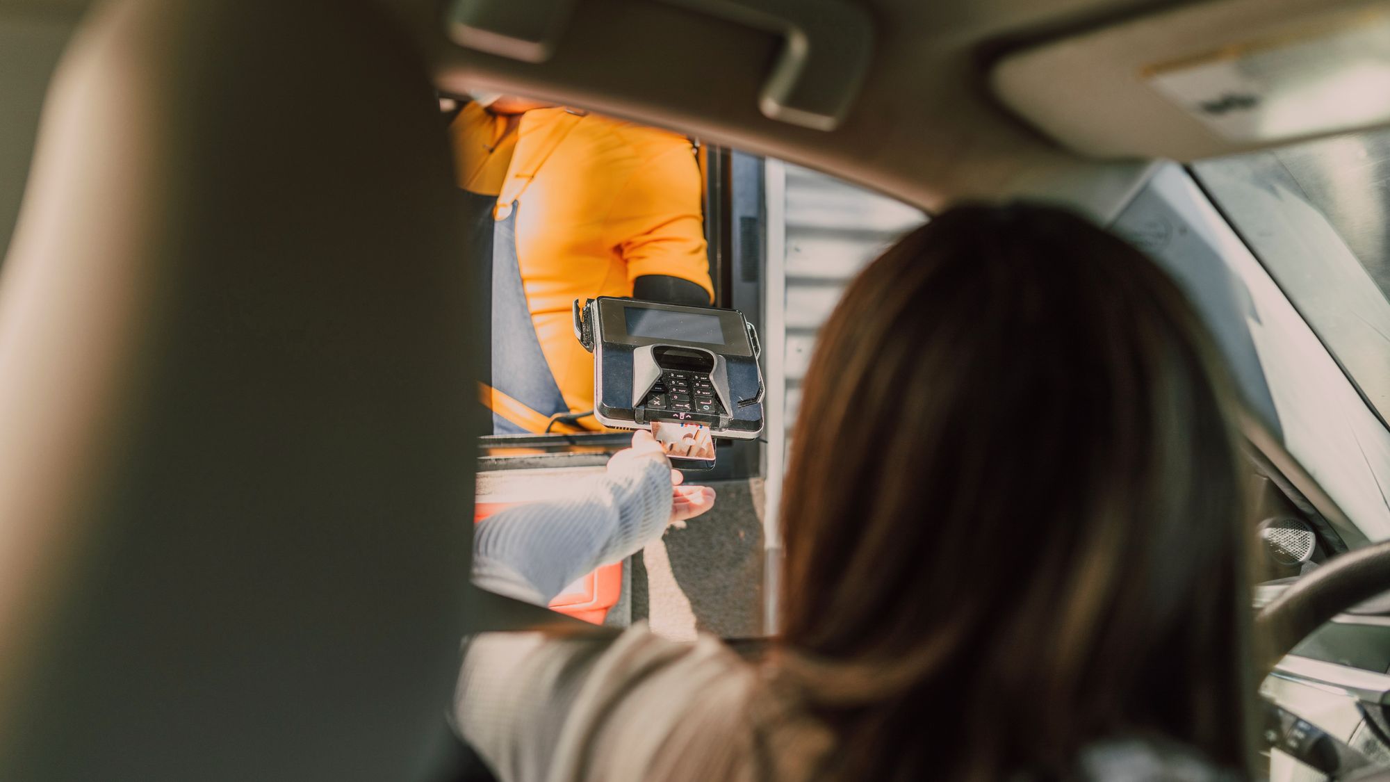 Au drive, une cliente en voiture paie avec le terminal que lui tend l’équipier à la fenêtre