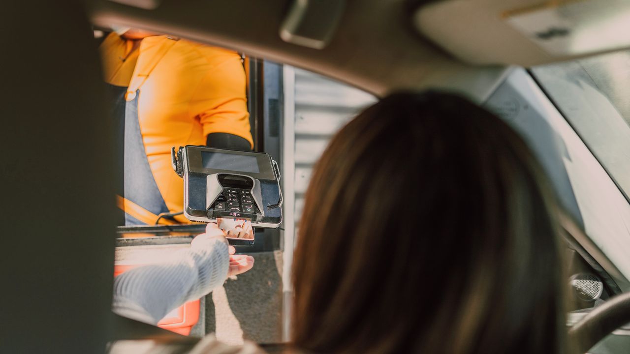 Au drive, une cliente en voiture paie avec le terminal que lui tend l’équipier à la fenêtre