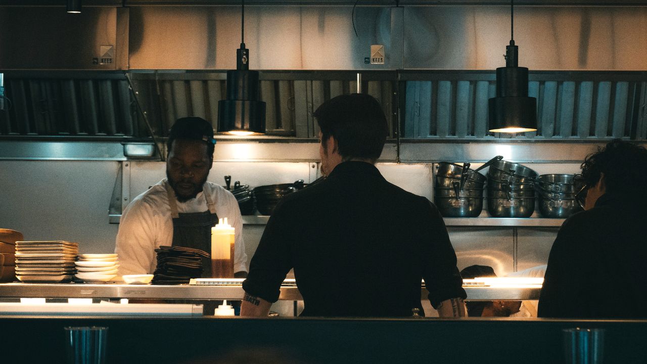 Équipe de cuisine au passe pendant le service du soir, sous les lampes, assiettes en préparation