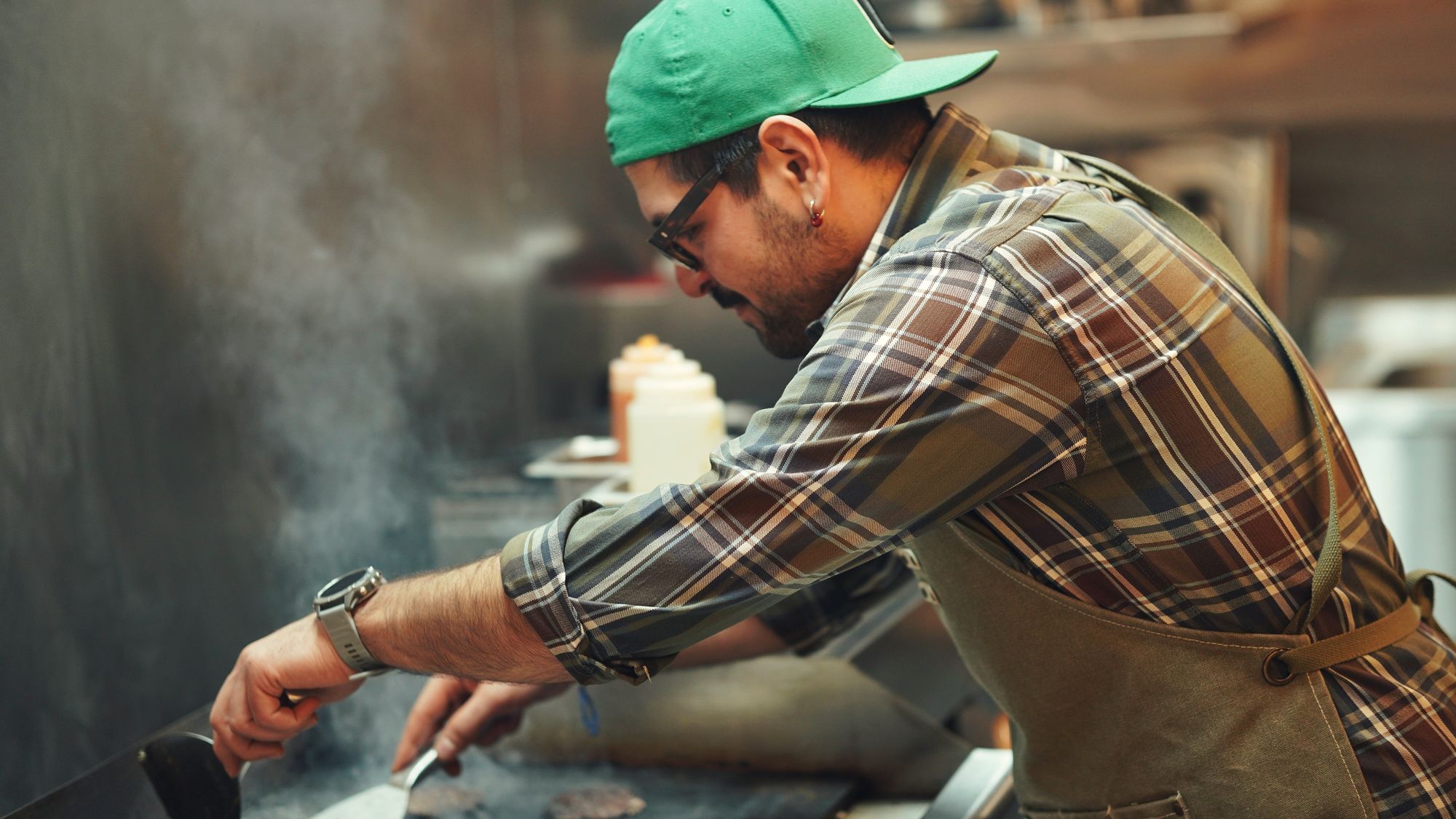Équipier au grill d’une cuisine de restauration rapide, en plein rush, steaks sur la plaque et vapeur