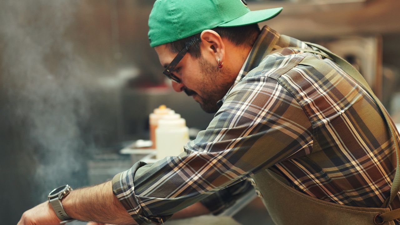 Équipier au grill d’une cuisine de restauration rapide, en plein rush, steaks sur la plaque et vapeur